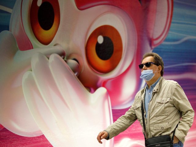 A commuter wearing a face mask or covering passes an advertisement depicting a monkey cove