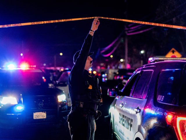 A Sacramento County Sheriff's Department officer holds up police tape to allow a vehicle t
