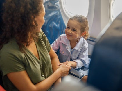 High angle view of little girl sitting on the plane, smiling to her mother while they are traveling together - stock photo