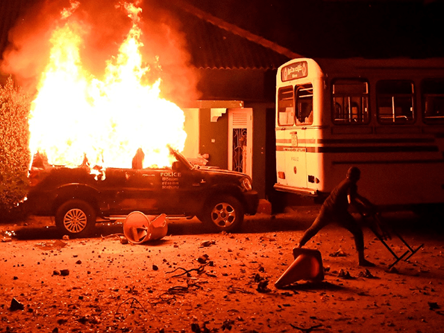 A protester throws an object at a bus next to a burning police car during a demonstration outside the Sri Lankan president's home to call for his resignation in Colombo on March 31, 2022. - Security forces were deployed across the Sri Lankan capital on April 1 after protesters tried …