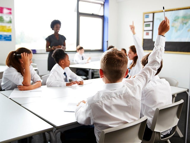 High School Students Wearing Uniform Raising Hands To Answer Question Set By Teacher In Classroom