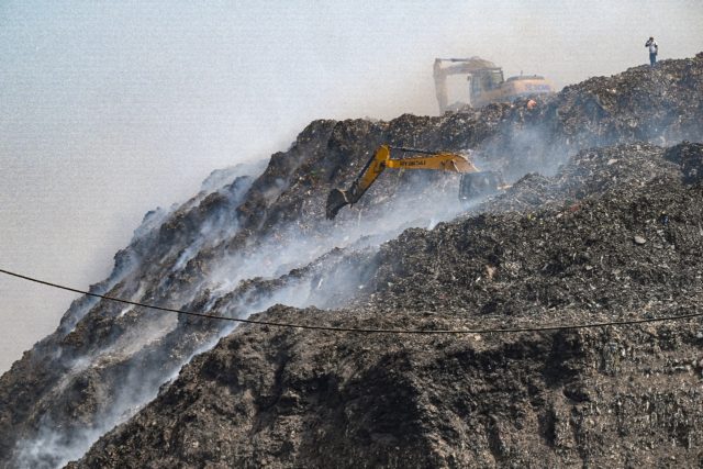 Workers operate excavators amidst burning garbage after a fire broke out at the Bhalaswa l