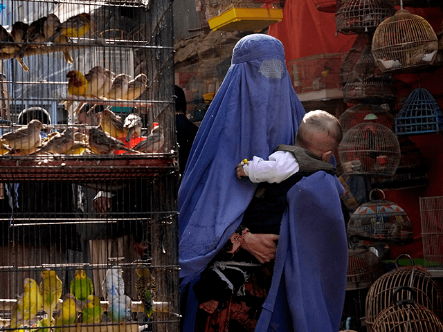 A woman wearing a burka walks through a bird market as she holds her child, in downtown Kabul, Afghanistan, Sunday, May 8, 2022.