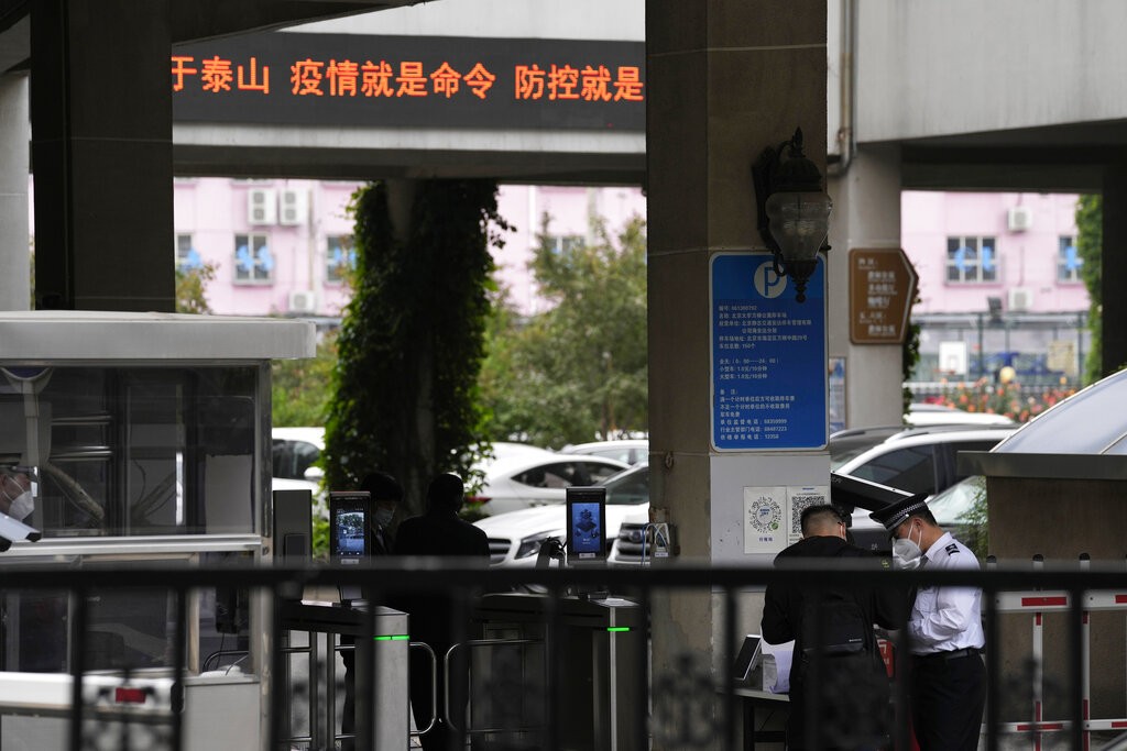 A security guard checks a man entering the Wanliu Campus of Peking University near a display showing slogans part of which reads 