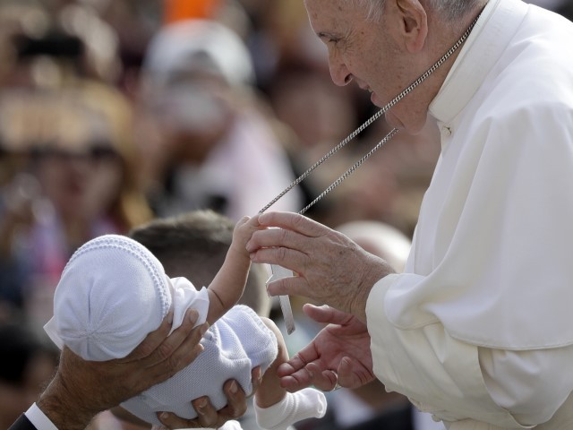 A baby handed over to Pope Francis to bless him clings to his cross as he arrives for his weekly general audience in St. Peter's Square, at the Vatican, Wednesday, September 25, 2019. 