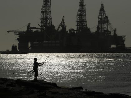 FILE - A man wears a face mark as he fishes near docked oil drilling platforms, on May 8,