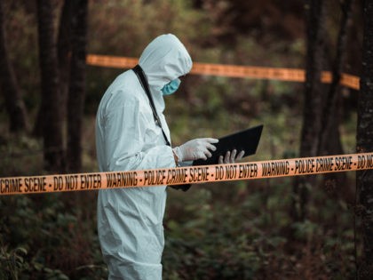 A forensic scientist is seen standing in a crime scene area while reading his notes. (FlyM