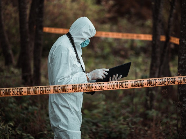 A forensic scientist is seen standing in a crime scene area while reading his notes. (FlyMint Agency/iStock/Getty Images Plus)