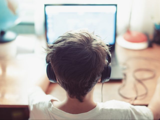 Little dependent gamer kid playing on laptop - stock photo
