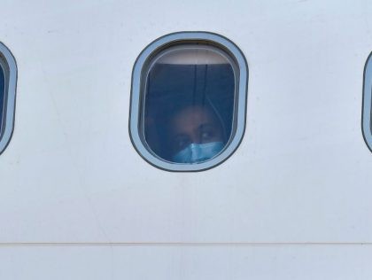 A minor migrant wearing a protective face mask looks through the window, after nearly 50 of them who were living in camps on the Greek islands boarded a plane at the International Airport of Athens, to travel on a special flight to Germany, on April 18, 2020. - Forty-nine minors …