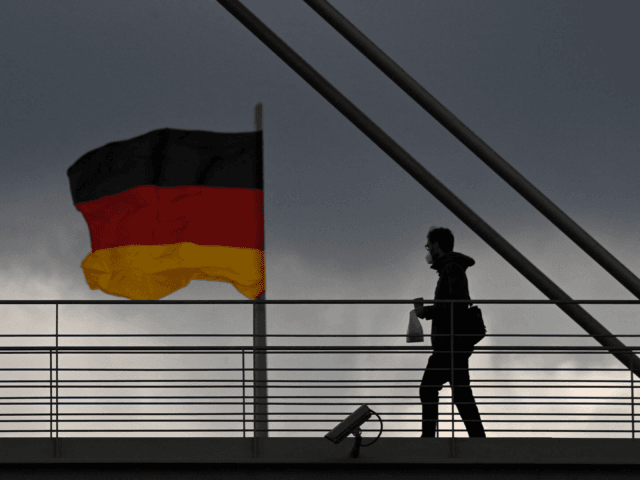 A man walks past the German flag as he crosses an overpass between two buildings of the parliamentary complex in Berlin on May 5, 2021, as dark clouds hang over the capital of Germany. (Photo by John MACDOUGALL / AFP) (Photo by JOHN MACDOUGALL/AFP via Getty Images)