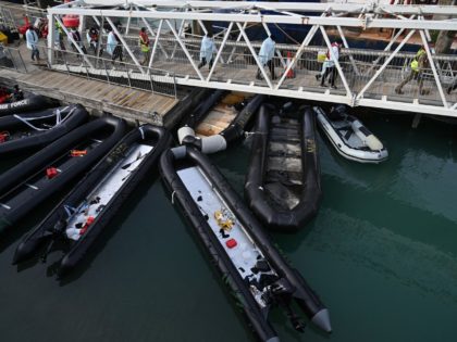 Walking above inflatable dinghies used by migrants, members of the British military help a group of migrants at the port of Dover after they disembark, having been picked up crossing the English Channel from France on April 14, 2022, at Dover, on the south-east coast of England. - Britain will …