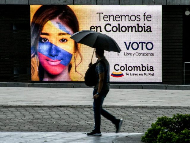 A man walks past a billboard that reads We have Faith in Colombia. Free and concious vote, in Medellin, Colombia, on May 28, 2022. - Colombians go to the polls Sunday in a deeply polarized election that could see a leftist -- and ex-guerrilla -- become president for the first time in the history of the violence- and inequality-plagued country. (Photo by JOAQUIN SARMIENTO / AFP) (Photo by JOAQUIN SARMIENTO/AFP via Getty Images)