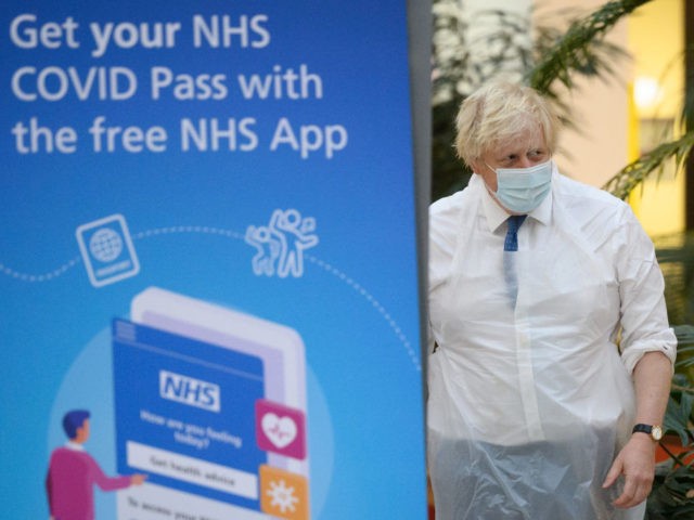 RAMSGATE, UNITED KINGDOM - DECEMBER 16: Britain's Prime Minister Boris Johnson walks past a poster advertising the NHS COVID Pass application, during a visit to an NHS Covid-19 vaccination centre on December 16, 2021 near Ramsgate, United Kingdom. The Government is pushing the booster jab program as the country recorded …