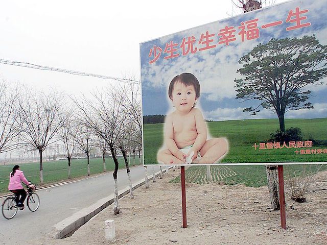 BEIJING, CHINA: A woman cycles pass a billboard encouraging couples to have only one child, along a road leading to a village in the suburb of Beijing, 25 March 2001. China has reaffirmed that it would continue enforcing its one-child policy to limit its huge population to 1.6 billion by 2050. AFP PHOTO/GOH Chai Hin (Photo credit should read GOH CHAI HIN/AFP via Getty Images)
