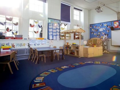 Landscape image of an empty, nursery classroom. there is a rug in the middle of the room.