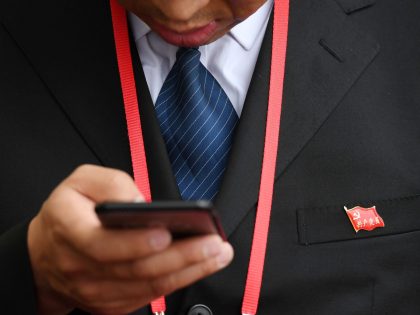 A delegate wearing a Communist Party badge looks at his smartphone during the opening ceremony of the 19th Communist Party Congress in Beijing's Great Hall of the People on October 18, 2017. President Xi Jinping declared China is entering a "new era" of challenges and opportunities on October 18 as …