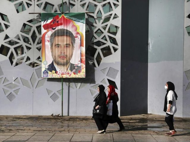 People walk past a banner showing Iran's Revolutionary Guard Col. Hassan Sayyad Khodaei who was killed on Sunday, prior to his funeral ceremony, in Tehran, Iran, Tuesday, May 24, 2022. Iran's hard-line President Ebrahim Raisi vowed revenge on Monday over the killing of Khodaei, who was shot at his car …