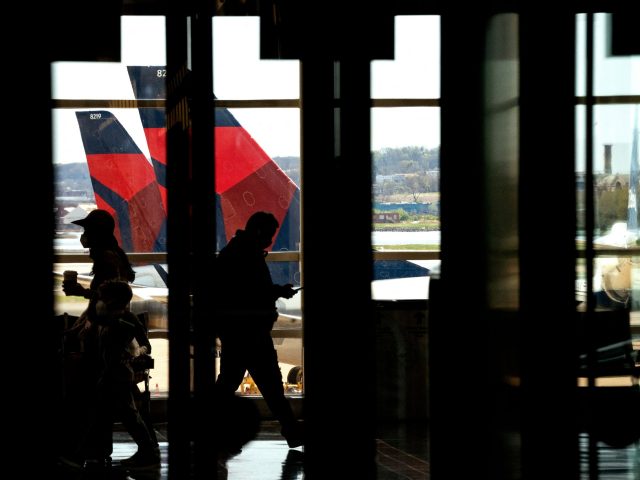 Delta Airlines aircrafts are seen in the background behind travelers passing through Ronald Reagan Washington National Airport in Arlington, Virginia on April 11, 2022. (Photo by Stefani Reynolds / AFP) (Photo by STEFANI REYNOLDS/AFP via Getty Images)