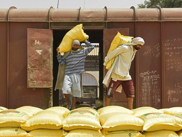 Labourers unload sacks of fertilizer from a train at a railway yard on a hot summer day on