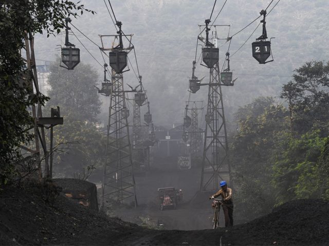 TOPSHOT - A worker pushes his bicycle under a line of cable trolleys transporting coal in