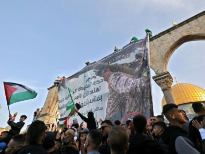 Supporters of the Palestinian Hamas movement wave Palestinian and Islamic flags in front of a banner depicting a fighter holding a hand-held anti-aircraft missile launcher as they rally by the Dome of the Rock mosque, at the Al-Aqsa Mosque complex in Jerusalem, after the morning Eid al-Fitr prayer, which marks …
