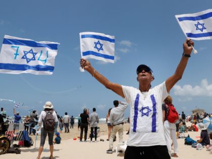An Israeli man waves flags as Israeli Efroni T-6 Texan II planes perform stunts in the sky above the Mediterranean coastal city of Tel Aviv on May 5, 2022, as Israel marks Independence Day (Yom HaAtzmaut), 74 years since the establishment of the Jewish state. - Israel's first prime minister …