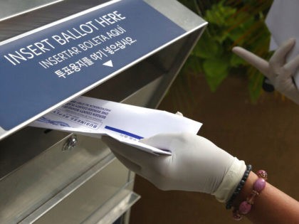 In this July 7, 2020, file photo a woman wearing gloves drops off a mail-in ballot at a dr