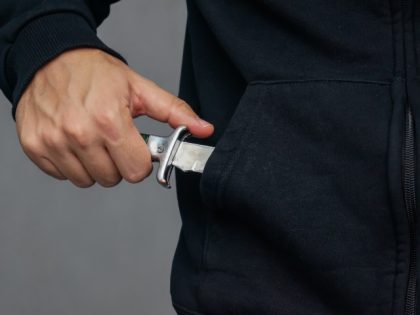 A man wearing a hoodie pulls a knife out of his pocket