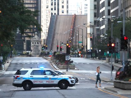 A pedestrian walks across Michigan Ave., Monday, Aug. 10, 2020, past a Chicago police department vehicle, a few blocks north of the raised Michigan Ave. bridge over the Chicago river after overnight vandalism in Chicago. Chicago’s police commissioner says more than 100 people were arrested following a night of looting …