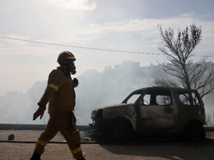 A firefighter walks next to a burnt car during a wildfire in Voula suburb, in southern Athens, Greece, Saturday, June 4, 2022. A combination of hot, dry weather and strong winds makes Greece vulnerable to wildfire outbreaks every summer. (AP Photo/Yorgos Karahalis)