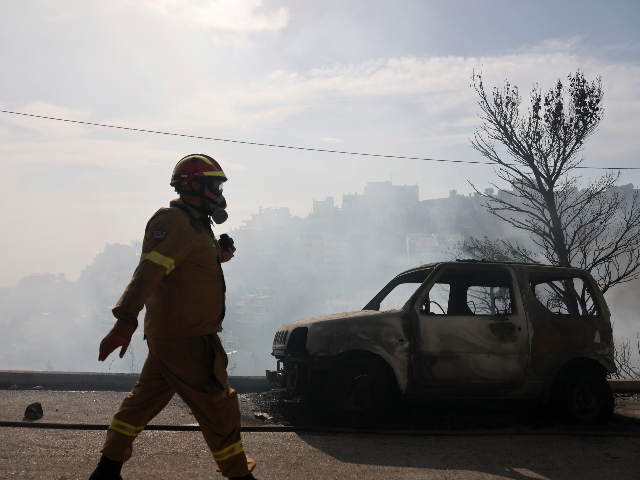 A firefighter walks next to a burnt car during a wildfire in Voula suburb, in southern Ath