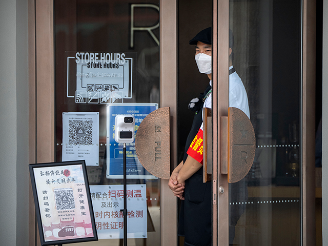 An employee wearing a face mask stands near a temperature scanner and QR codes for health apps as they wait for customers at a cafe along a tourist shopping street in Beijing, Saturday, June 18, 2022. China on Friday defended its tough "zero-COVID" policy after the U.S. ambassador said it …