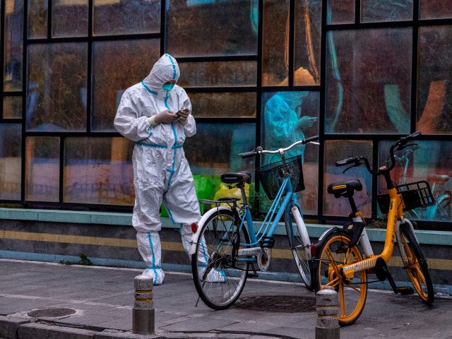BEIJING, CHINA -JUNE 13: A health worker wears protective clothing as he looks at his phone near a community that is locked down, after a recent COVID-19 outbreak on June 13, 2022 in Beijing, China. China’s capital is working to control a fresh COVID-19 cluster after dozens of people linked …