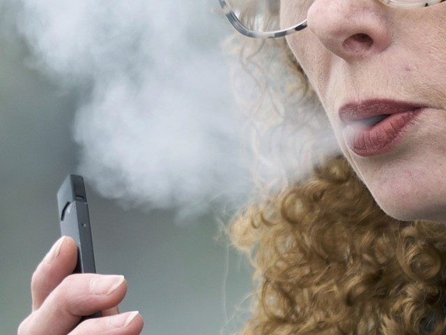 FILE - In this April 16, 2019, file photo, a woman exhales while vaping from a Juul pen e-cigarette in Vancouver, Washington. On Wednesday, Feb. 12, 2020, Massachusetts sued Juul Labs Inc., accusing the company of deliberating targeting young people through its marketing campaigns. (Craig Mitchelldyer, File/AP)