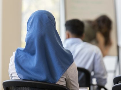 In this closeup rear view, an unrecognizable woman wearing a hijab sits in a chair in a cl