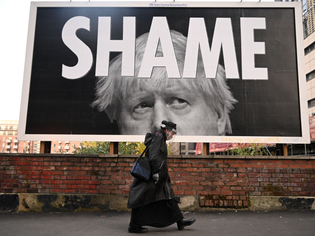 TOPSHOT - A woman wearing a protective face shield passes a billboard showing Britain's Pr