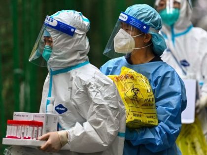 Health workers walk holding swab samples taken from people next to the entrance of a residential area under Covid-19 lockdown in the Xuhui district of Shanghai on June 10, 2022. (Photo by Hector RETAMAL / AFP) (Photo by HECTOR RETAMAL/AFP via Getty Images)