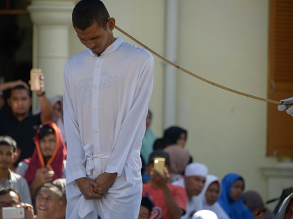 Graphic content / A member of Indonesia's Sharia police (R) whips a man (L) accused of having gay sex during a public caning ceremony outside a mosque in Banda Aceh, capital of Aceh province on July 13, 2018. - A gay couple was publicly whipped in Indonesia's conservative Aceh province …