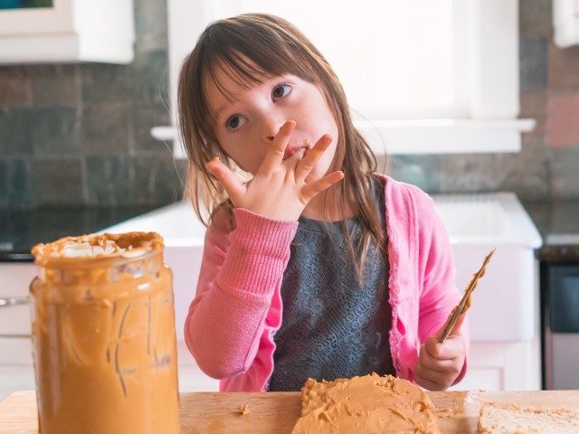 Girl making peanut butter sandwich, licking fingers (Getty)