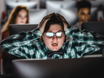 Shocked nerdy student having problems while e-learning over desktop PC at computer lab.