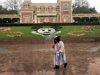 ANAHEIM, CA - MARCH 12: A Disneyland employee walks through the entrance to Disneyland amid rain showers in Anaheim, Calif., on March 12, 2020. Disneyland will temporary close the Disneyland Resort in Anaheim in response to the expanding threat posed by the Coronavirus Pandemic. The closure takes effect Saturday and …