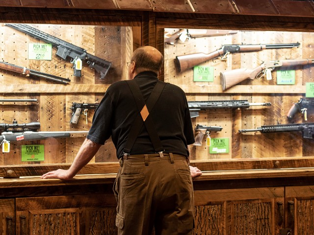 In this April 25, 2019, file photo, a man looks at cases of firearms in the halls of the Indianapolis Convention Center where the National Rifle Association will be holding its 148th annual meeting in Indianapolis. The number of background checks conducted by federal authorities is on pace to break a record by the end of this year. (AP Photo/Lisa Marie Pane, File)