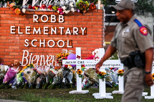 Police officers walk past a makeshift memorial for the shooting victims at Robb Elementary