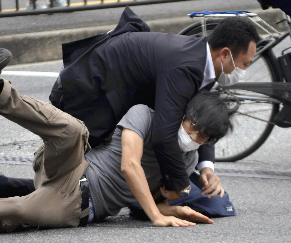 Tetsuya Yamagami, bottom, is detained near the site of gunshots in Nara Prefecture, western Japan, Friday, July 8, 2022. Former Japanese Prime Minister Shinzo Abe, a divisive arch-conservative and one of his nation's most powerful and influential figures, has died after being shot by Yamagami during a campaign speech Friday in western Japan, hospital officials said.(Katsuhiko Hirano/The Yomiuri Shimbun via AP)