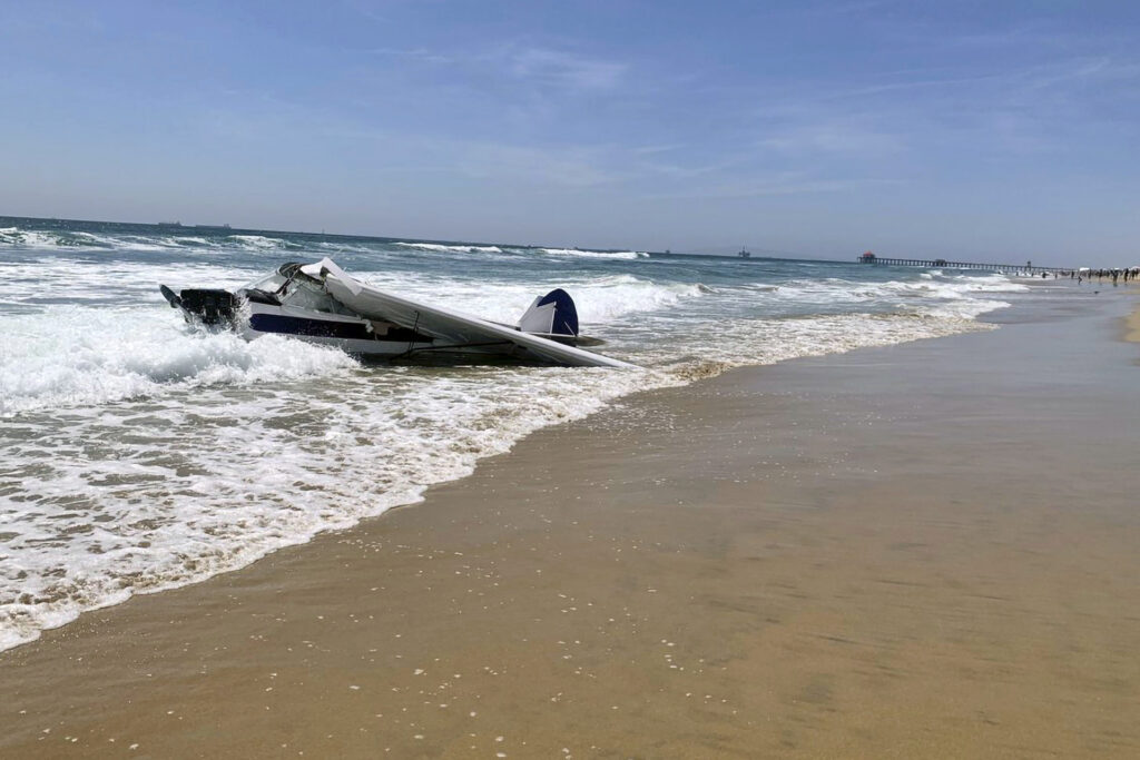 In this image provided by the Huntington Beach Fire Department, a small plane sits in the surf after it crashed into the ocean just off Huntington Beach, Calif., on Friday, July 22, 2022, during a lifeguarding competition. A Coast Guard spokesperson says the plane went down Friday about 30 yards from shore and the pilot was rescued. He was the only person aboard. (Huntington Beach Fire Department via AP)