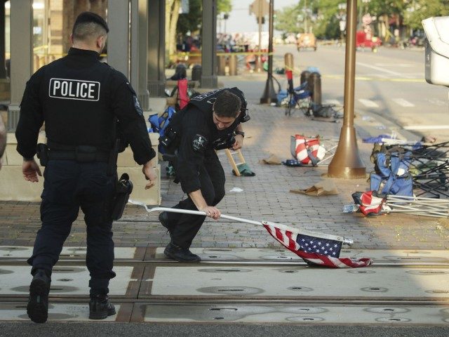 A police officer picks up a waterlogged American flag, Tuesday, July 5, 2022, left behind after Monday’s mass shooting in Highland Park. (Stacey Wescott/Chicago Tribune/Tribune News Service via Getty Images)