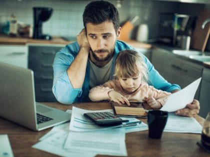 A father, worried about finances, works on paying bills with his little daughter in his lap. (Getty)