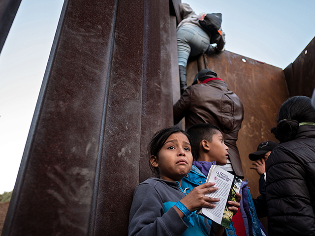 A Central American migrant girl holds a book as other migrants travelling in a caravan, climb the Mexico-US border fence in an attempt to cross to San Diego County, in Playas de Tijuana, Baja California state, Mexico on December 12, 2018. - Thousands of Central American migrants have trekked for …