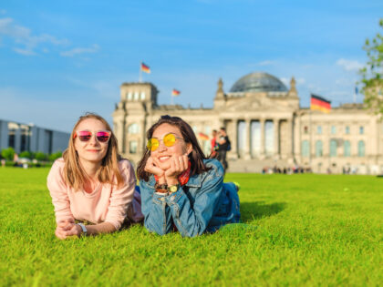 Two Young happy girls wearing sun glasses lying on a grass and have fun in front of the Bundestag building in Berlin. Studying abroad and travel in Germany concept
